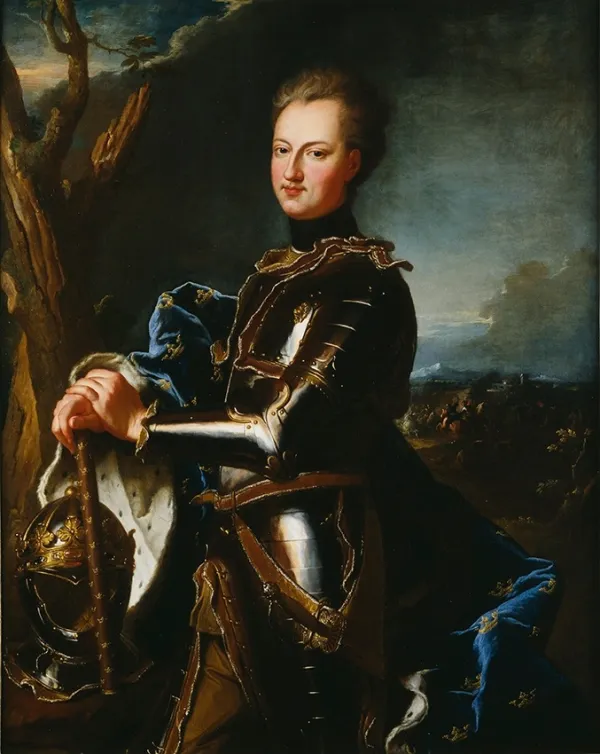 An oil portrait of a young man in dark polished armour with gilt edging, a blue ermine-lined cloak strewn with gold crowns over one shoulder, both hands resting on a baton above a plumed helmet, a tree behind him at the left and a distant cavalry engagement at the right
