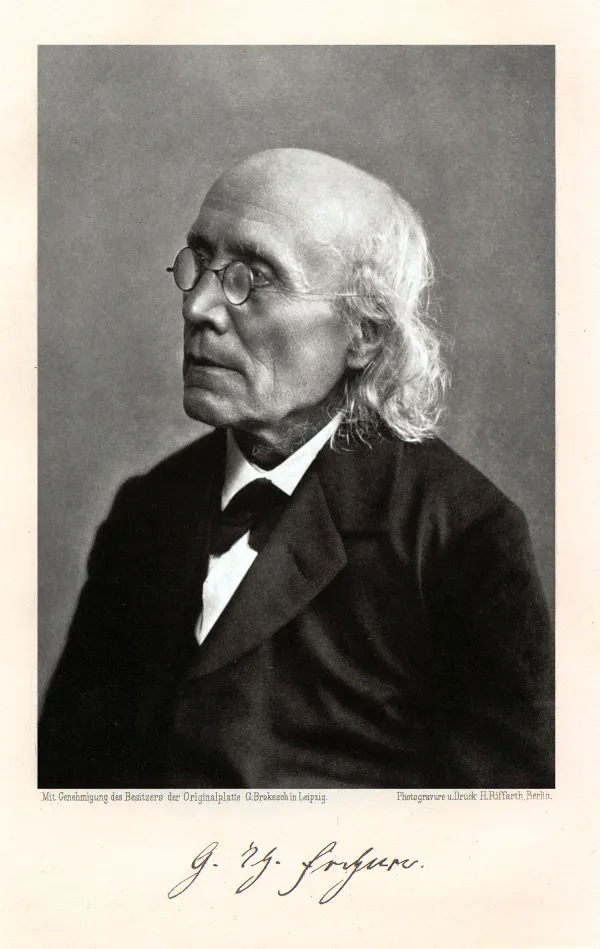 A photogravure portrait of an elderly man in three-quarter profile: bald over the crown with long white hair falling past his ears, oval wire-rimmed spectacles, a dark coat over a white collar and a dark bow, against a plain grey ground. A facsimile signature is printed beneath