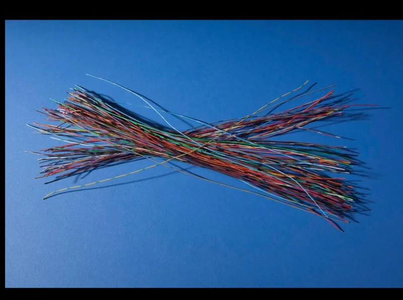 A framed photograph on a blue ground of a loose bundle of many short lengths of brightly coloured insulated wire, red, blue, green, yellow and white, crossing each other in a broad X