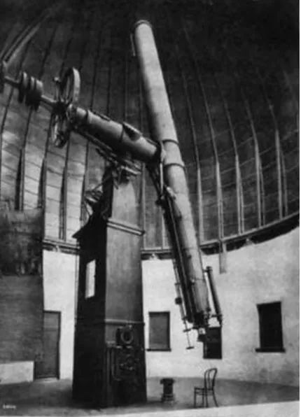 A black-and-white photograph of a large refracting telescope inside its observatory dome: a long tube on an equatorial mounting atop a tall square masonry pier, angled up to the left, with a bentwood chair and a small stool on the floor beside it for scale